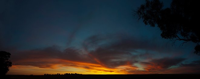 An orange sunset lights up the clouds in this rural country panorama.