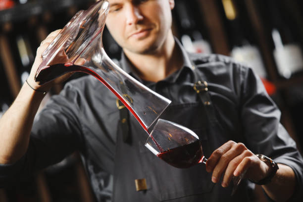 istock Bartender pours red wine in glass from big transparent vessel 1224141922