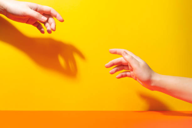 istock Two hands reach for each other with fingers. Shadows and hard light 1224146069
