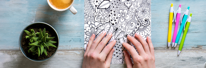 Adult coloring book, stress relieving trend. Art therapy, mental health, creativity and mindfulness concept. Flat lay close up on woman hands coloring an adult coloring book banner.