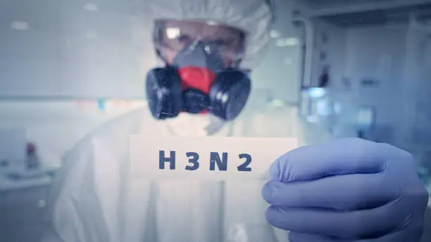 Photo of Word 'H3N2' set on fire in laboratory. Healthcare worker with gas mask