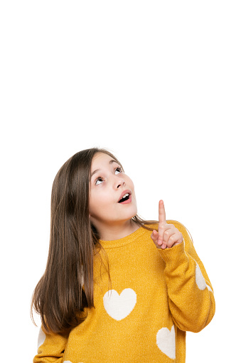 Beautiful young girl in mustard yellow sweater looking and pointing up. Waist up studio shot on white background.
