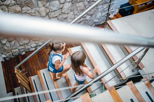 High angle view of 6 and 8 year old sisters walking up stairs to second story of modern family home.