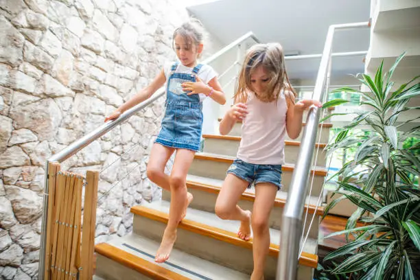 Photo of Young Sisters Coming Down Stairs in Modern Family Home