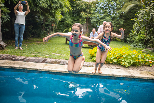 Young Girls Jumping into Family Swimming Pool