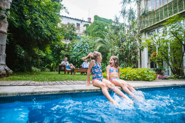 istock Hispanic Sisters Sitting on Side of Pool and Splashing 1224153031