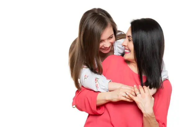 Photo of Waist up studio portrait of cute and playful schoolgirl embracing her mother. Happy family laughing background isolated over white.