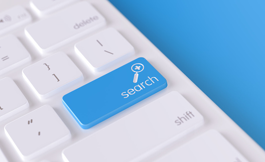 Search text and magnifying glass icon written on a blue button of a computer keyboard. Horizontal composition with selective focus and copy space. High angle view. Search concept.