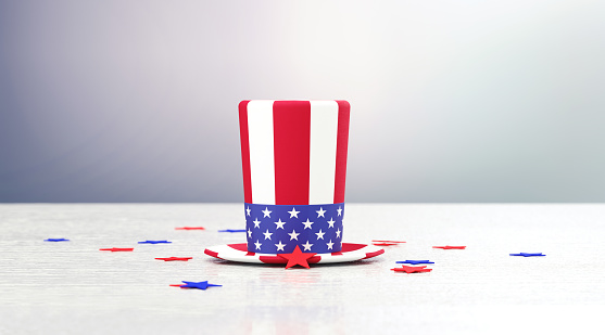 Patriotic American hat textured with American flag and surrounded by star shaped confetti sitting on wood surface in front of defocused  background. Horizontal composition with copy space. Front view. 4th of July - Independence Day concept.