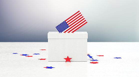 Ballot box and vote textured with American flag and surrounded by star shaped confetti sitting on wood surface in front of defocused  background. Horizontal composition with copy space. Front view.