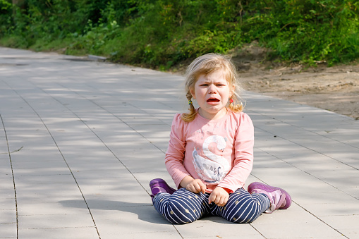 Cute upset unhappy toddler girl crying. Angry emotional child shouting. Portrait of kid with tears. Girl sitting on ground at crying.