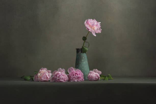 istock Vintage pottery vase with one peony and some peonies lying next to it on a table in a grey room. 1224157112