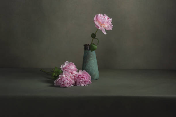 istock Vintage pottery vase with one peony and some peonies lying next to it on a table in a grey room. 1224157113