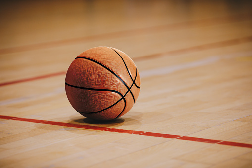 A shot of a single basketball resting on the floor in an indoor basket ball court. There are no people in the shot