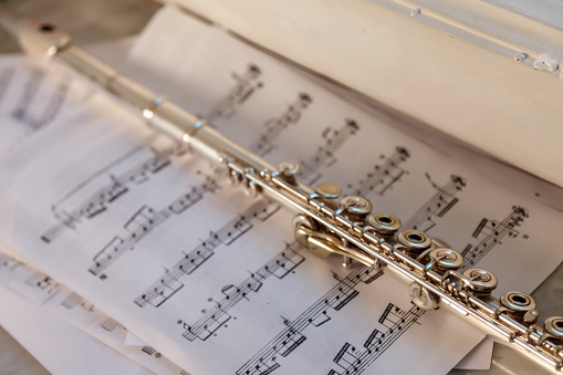 Flute And Sheet Music. Cross flute on a sheet of music. Silver flute on an old musical background. Classical soprano saxophone, on the windowsill with musical notes