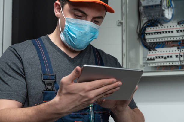 electrician with n95 face mask using digital tablet in front fuse box - cell human cell plant cell virus imagens e fotografias de stock