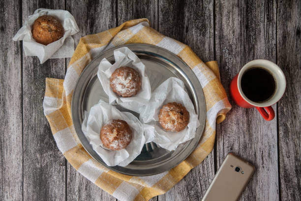 muffin su una piastra di metallo e caffè in una tazza di ceramica rossa, accanto a uno smartphone su uno sfondo di legno. lay piatto. vista dall'alto - coffee muffin pastry blueberry muffin foto e immagini stock