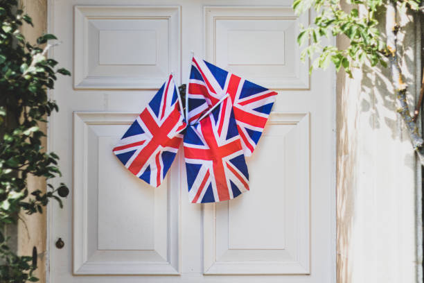 Union Jack Flags hanging from a door outside an old Cotswold house to celebrate  the 75th anniversary Victory in Europe’ VE celebrations. Union Jack Flags hanging from a door outside an old Cotswold house to celebrate  the 75th anniversary Victory in Europe’ VE celebrations. ve day celebrations uk stock pictures, royalty-free photos & images