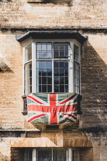 Union Jack Flag hanging from an old Cotswold stone terraced bay window to celebrate the 75th anniversary Victory in Europe’ VE celebrations.