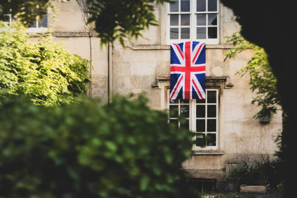 Union Jack Flag hanging from an old Cotswold stone terraced window to celebrate  the 75th anniversary Victory in Europe’ VE celebrations. Union Jack Flag hanging from an old Cotswold stone terraced window to celebrate  the 75th anniversary Victory in Europe’ VE celebrations. ve day celebrations uk stock pictures, royalty-free photos & images