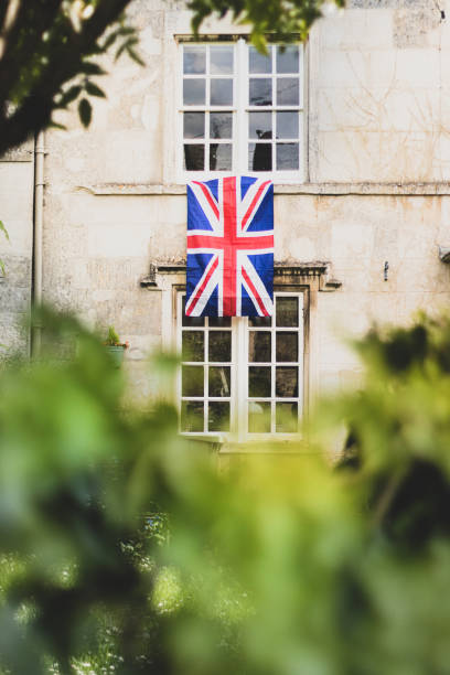 Union Jack Flag hanging from an old Cotswold stone terraced window to celebrate  the 75th anniversary Victory in Europe’ VE celebrations.