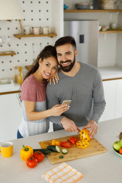 istock Young woman using her smart phone while her boyfriend prepares a meal 1224172186