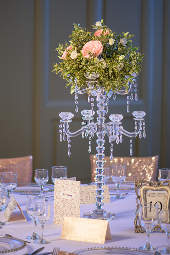 Elegant table arrangement for a formal event, a wedding or a fine dining experience, featuring a gorgeous centerpiece, a crystal candelabra candlestick with a roses and greenery bouquet in the middle.