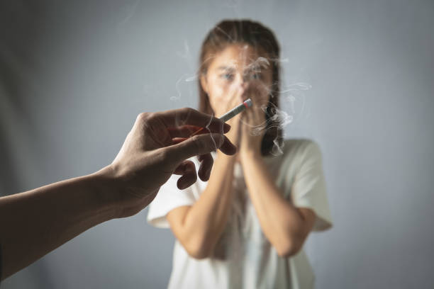Hand of Man is smoking cigarette and woman is covering her face. Passive smoking concept. stock photo