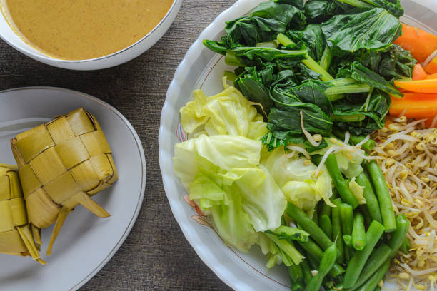 Pecel before mixing, indonesian traditional food made from various boiled vegetables such as carrots, bean sprouts, cabbage, long beans, mustard greens served with peanut sauce and ketupat