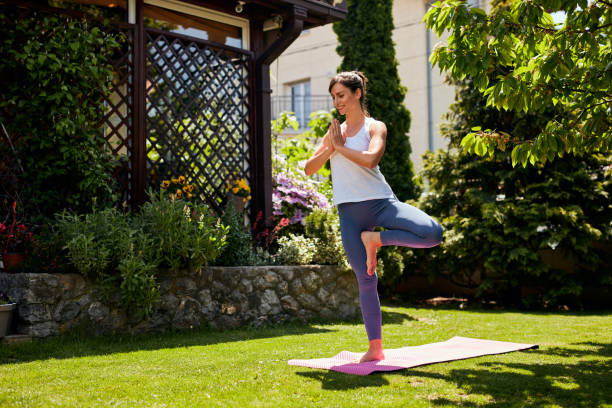 istock Young attractive brunette standing on the mat in her backyard in tree position. 1224179051