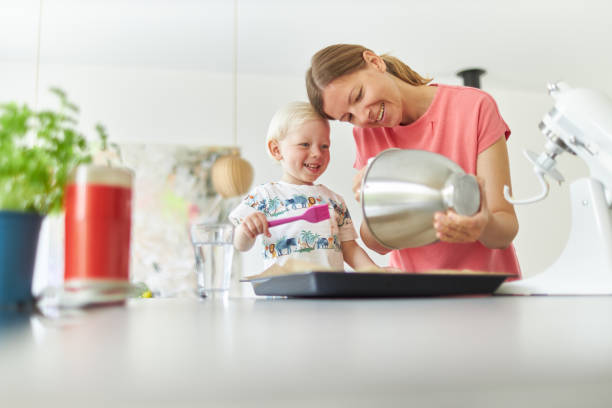 une mère fait cuire du pain avec son petit fils aux cheveux blonds dans sa cuisine moderne et lui apprend à faire fonctionner le robot culinaire et se laver les mains correctement après avoir fini la pâte. - wash bowl photos et images de collection