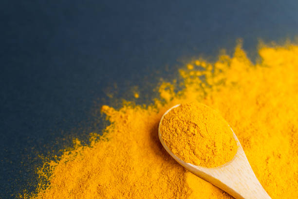 polvere di curcuma ravvicinata in cucchiaio di legno alla curcuma sparsa. - spice ayurveda herb curry powder foto e immagini stock