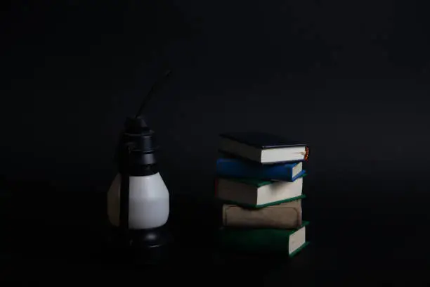 a pile of books and a petrol-lamp isolated on black background horizontal image. Image contains copy space