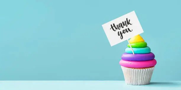 Brightly colored rainbow cupcake decorated with a thank you sign