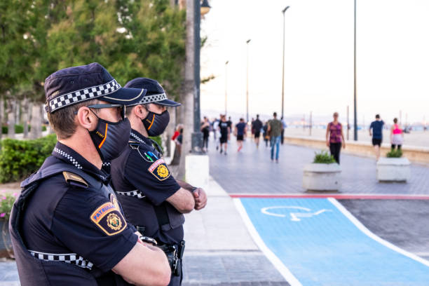 A couple of police officers monitor security measures while people walk and play sports during the coronavirus confinement on the promenade of Valencia, Spain. stock photo