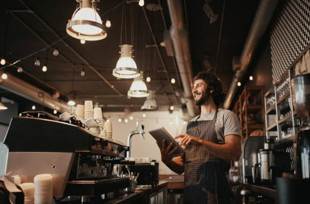 istock Smiling caucasian man wearing apron standing behind cafe counter using digital tablet looking away 1224190317