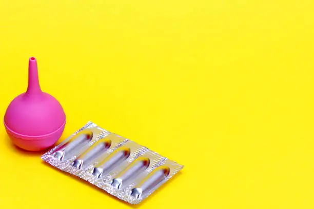 Medical new enema. Enema in medicine. Medical suppositories in a silver blister pack and a pink rubber medical enema on a yellow background. Packaging of contraceptives, vaginal, rectal candles.
