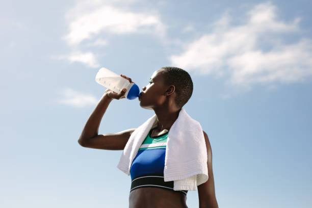 Fitness woman drinking water against sky Fitness woman drinking water against sky.  Female athlete drinking water outdoors after training session. healthy lifestyle women outdoors athlete stock pictures, royalty-free photos & images