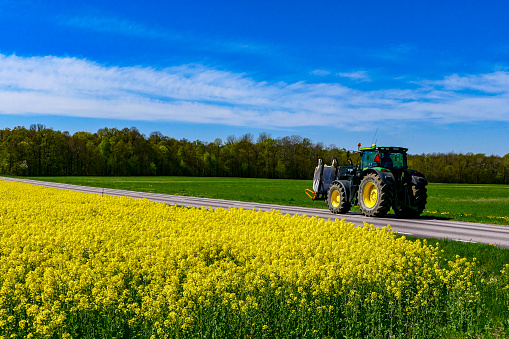 Farjestaden, Oland, Sweden May 10, 2020 An agricultural tractor driving on a back road next to a field of rapeseed.