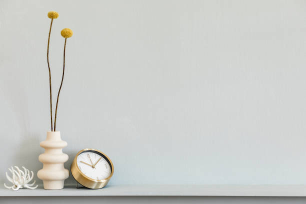 istock Minimalistic composition on the shelf with dried flower in design vase, gold clock and decoration on the stylish living room interior. Grey wall. Copy space. 1224196043