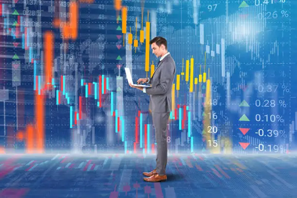 Photo of Businessman holding laptop in front of stock market data background