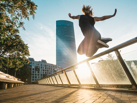 A woman jumping in the city, in front of a skyscraper, Bilbao, Spain
