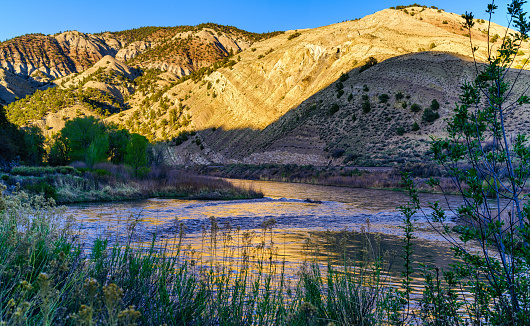 Colorado River with Golden Hour Reflections in Water - Scenic river landscape in rugged red rock canyon.