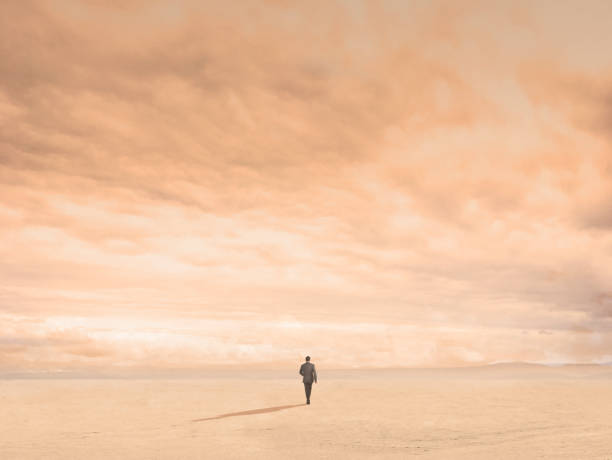 Man On A Lonely Walk A lone man walks toward the distant horizon. The scene evokes an emptiness and loneliness that is magnified by the stark and barren nature of the surroundings. horizon over land stock pictures, royalty-free photos & images