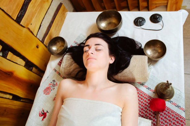 a beautiful brunette in relaxation lies on her back among the singing bowls. meditation session in progress. singing thickets, punitive and gong, a bell lie nearby. ethnic style. mysticism concept stock photo