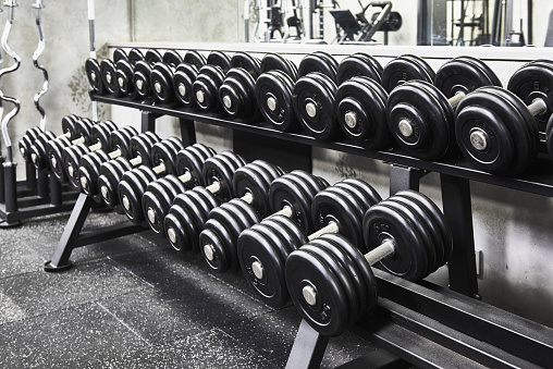 Rows of metal heavy dumbbells on rack in the sport gym, monochrome color tone. Sports equipment for weight training.