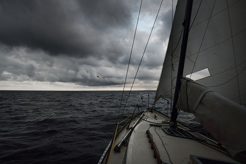 Modern small 24 feet racing sloop rigged yacht sailing in a thunderstorm. Terrific cloudscape. Dark storm sky. Baltic sea, Latvia