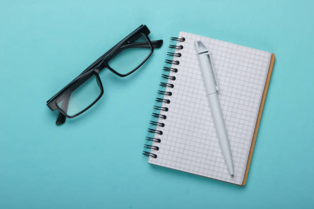 istock Classic eyeglasses and notebook with pen on a blue pastel background. Top view 1224208350