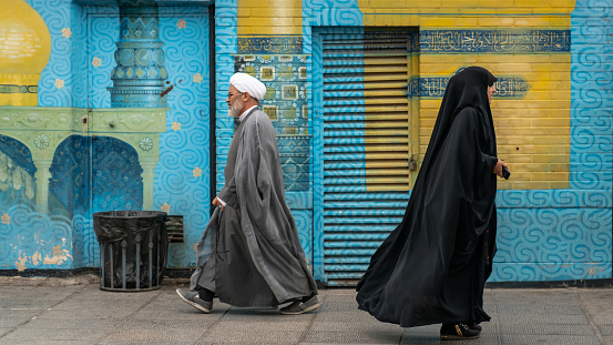 Qom, Iran - May 2019: Iranian man and woman in black dress walking in a street in the sacred city of Qom