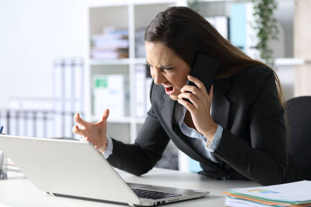istock Angry executive calling on phone looking at laptop at office 1224209024